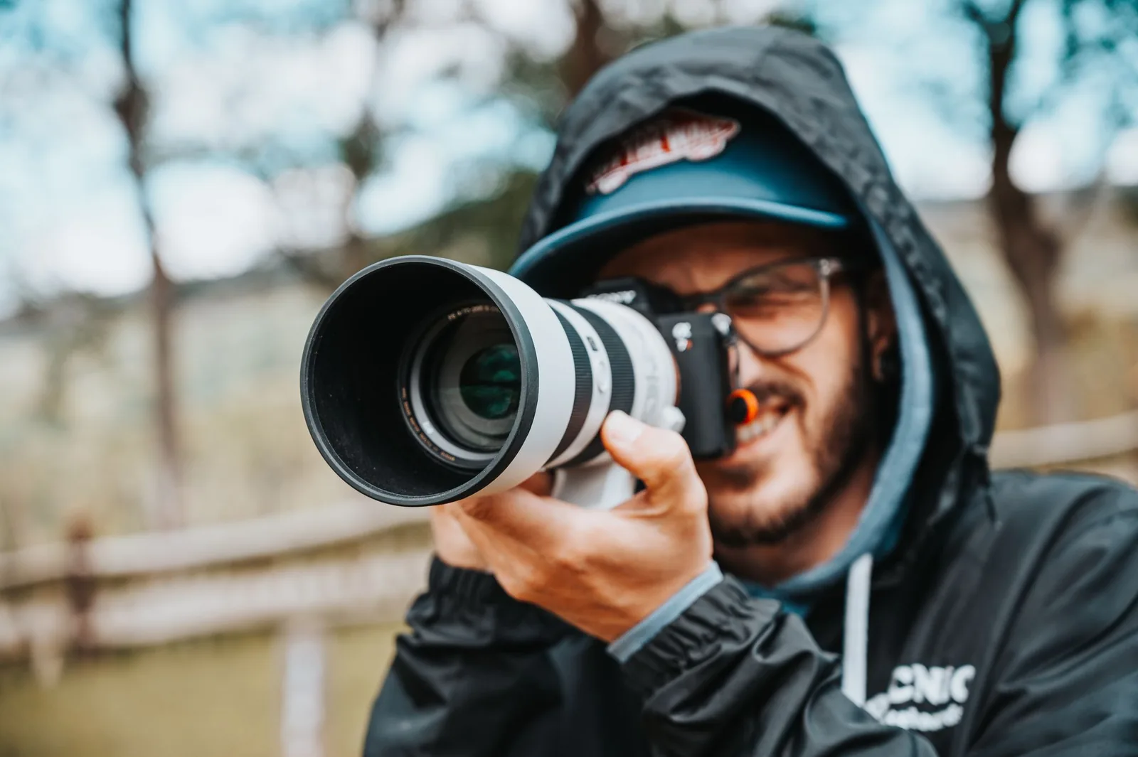 Fotograf care lucrează în aer liber, cu aparatul la ochi