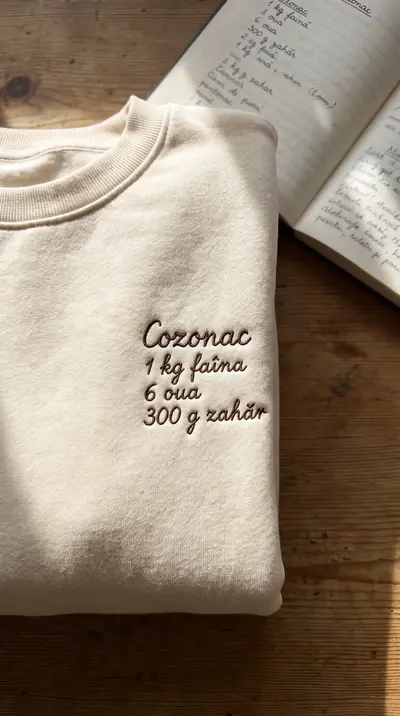 Bluză crem cu o rețetă de cozonac brodată în scris de mână, lângă caietul de bucătărie