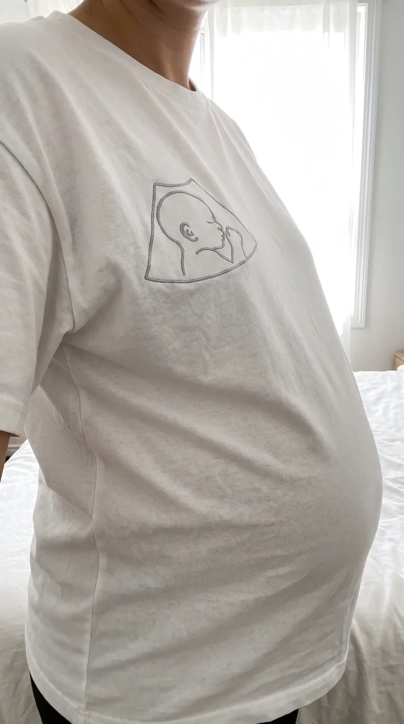 Tricou alb purtat peste burtica de gravidă, cu conturul ecografiei brodat