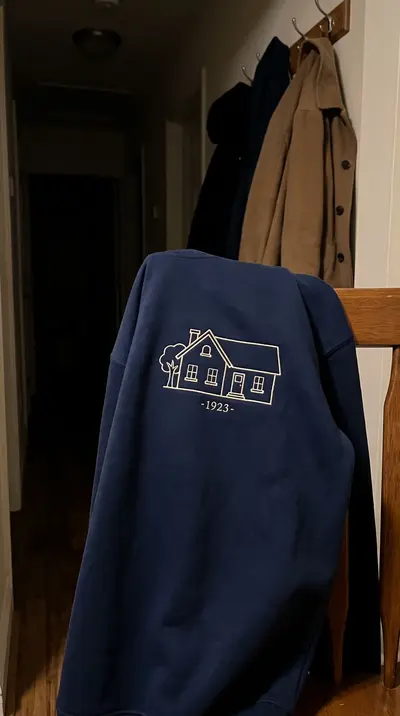Bluză bleumarin pe un scaun, cu conturul unei case brodat cu fir crem